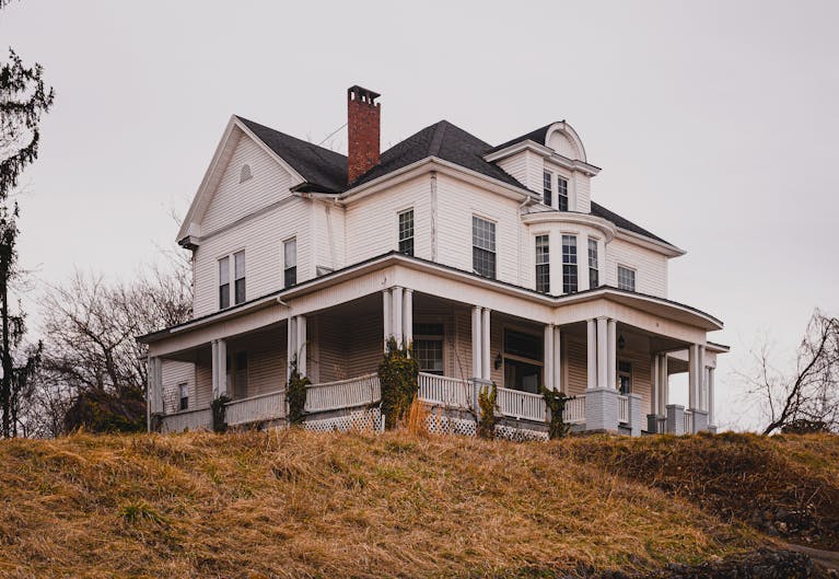 Beautiful historic white house with a wraparound porch set against autumn surroundings.