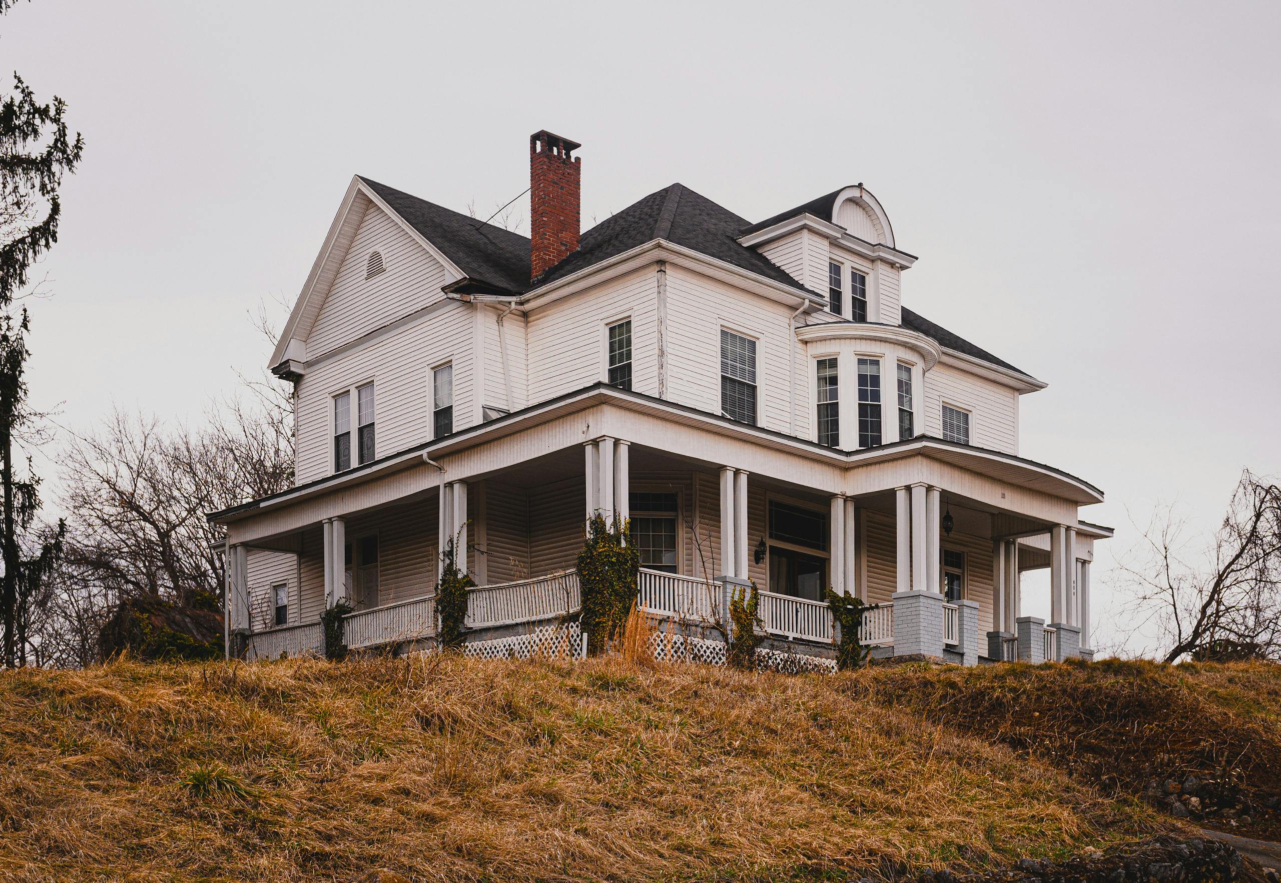 Beautiful historic white house with a wraparound porch set against autumn surroundings.